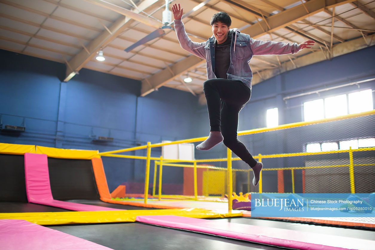 Happy young Chinese man jumping on trampoline