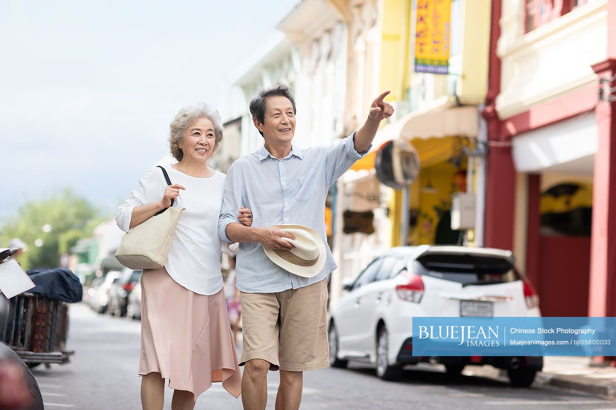 Happy senior Chinese couple walking on street