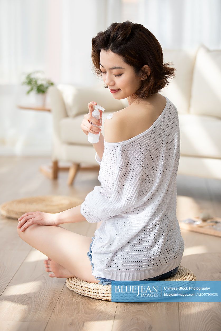 Happy young Chinese woman applying moisturizer at home