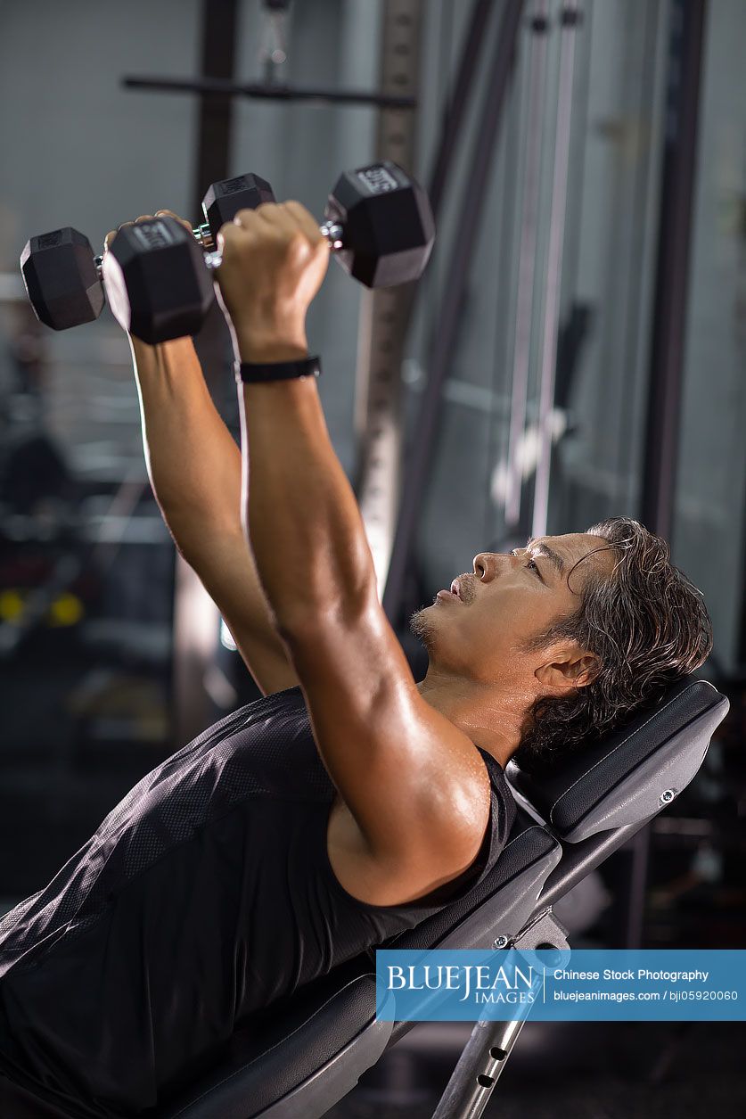 mature-chinese-man-working-out-with-hand-weights-at-gym-high-res-stock