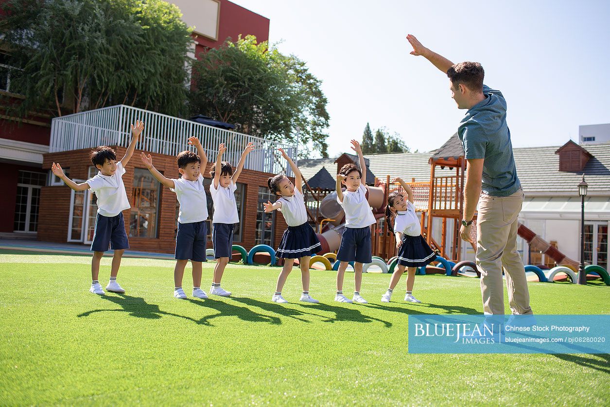 Foreign teacher and children exercising in playground