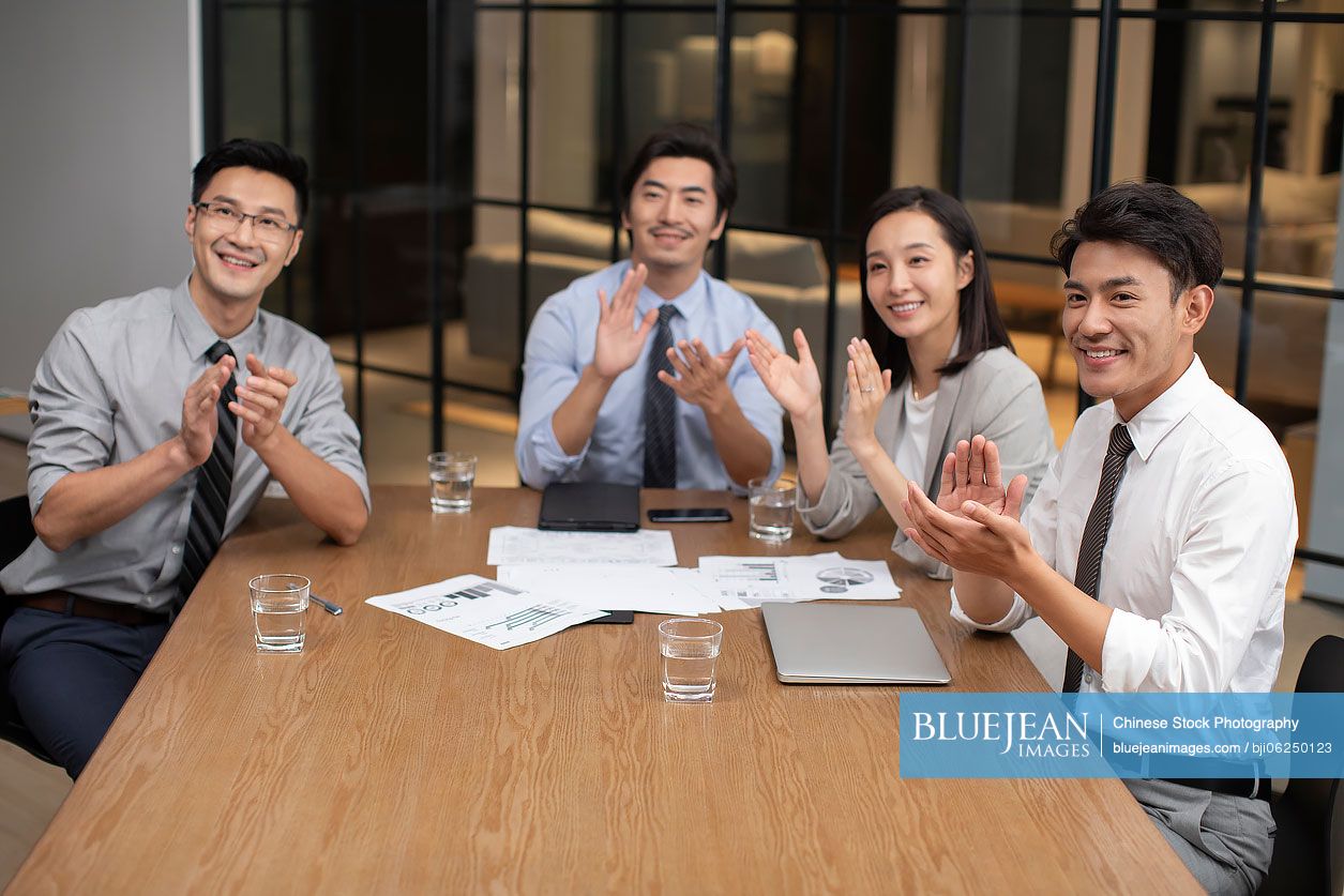 Chinese business people clapping hands in meeting room