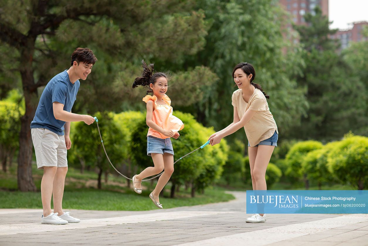 Happy young Chinese family jumping rope in park