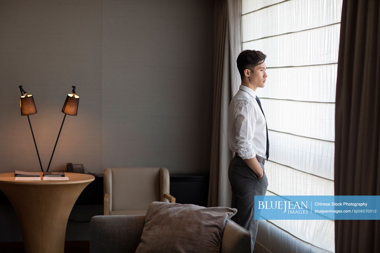 Young Chinese businessman thinking in front of hotel window