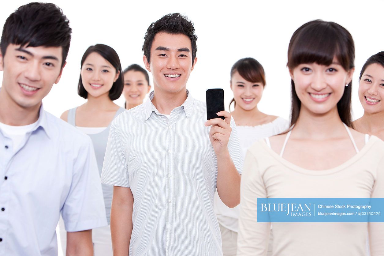 Portrait of young Chinese man showing mobile phone with friends around