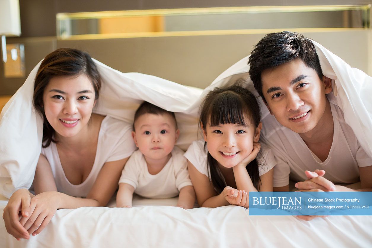 Happy young Chinese family lying on bed-High-res stock photo for download