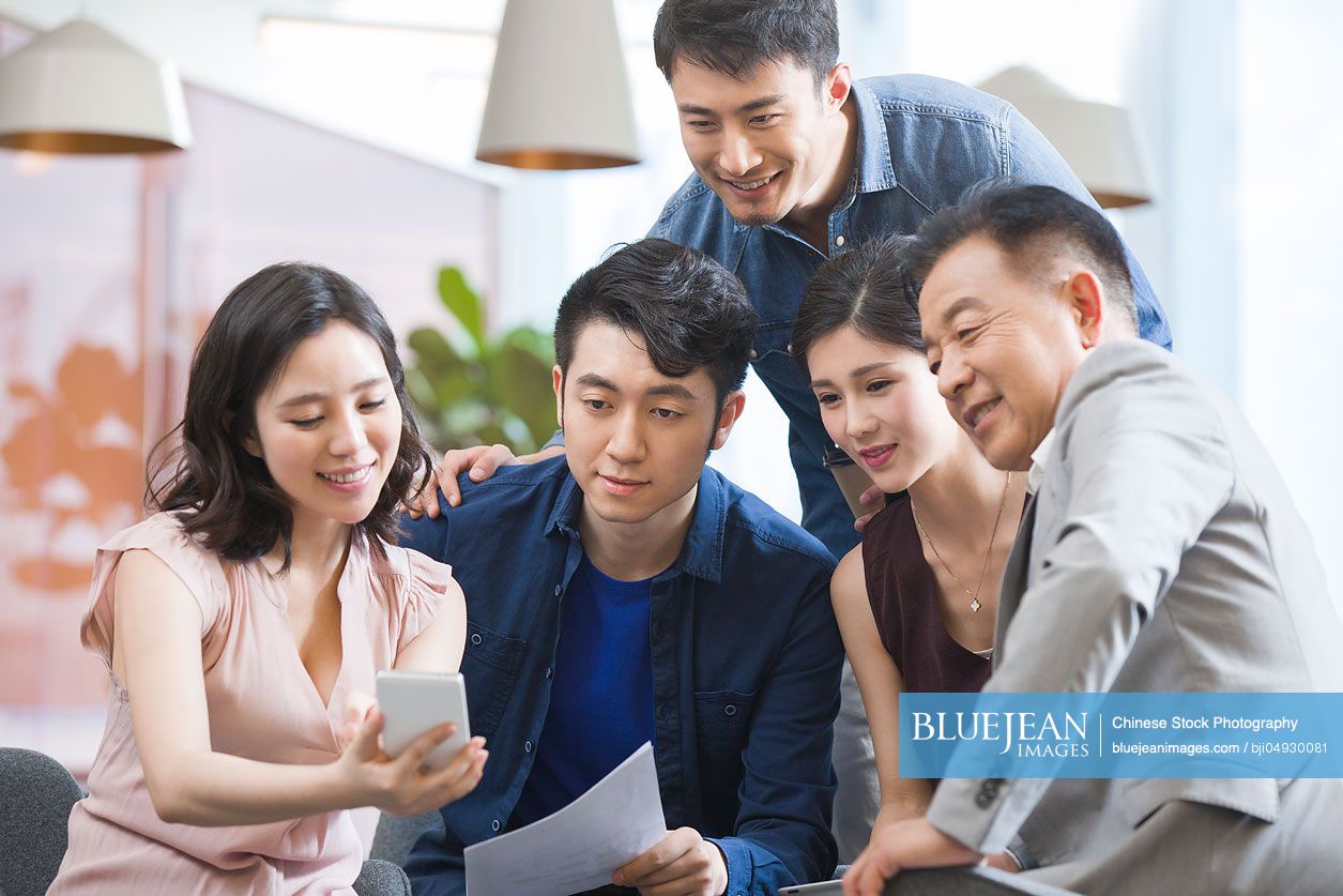 Chinese businesswoman showing smart phone to colleagues