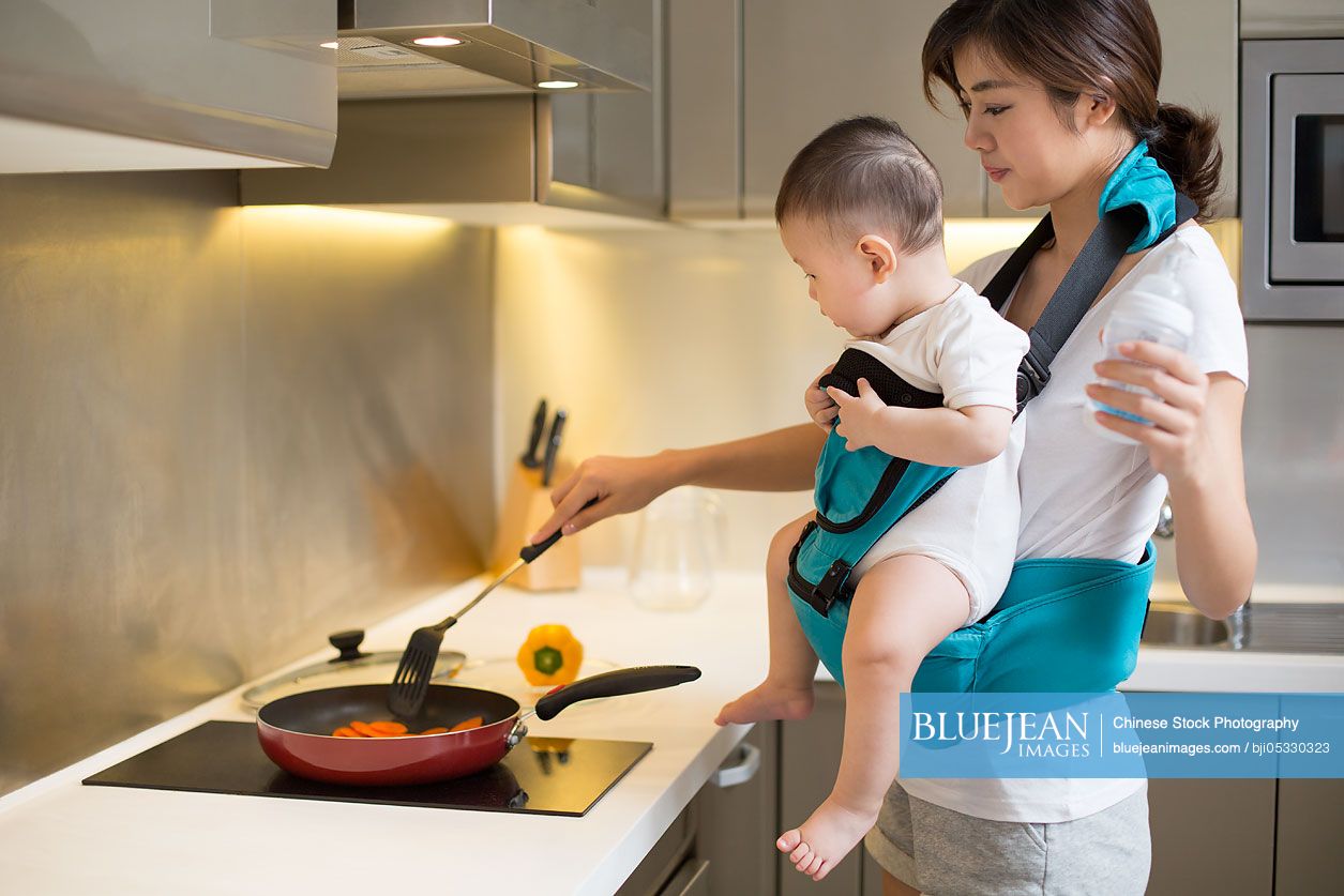 Chinese mother holding baby and cooking in the kitchen