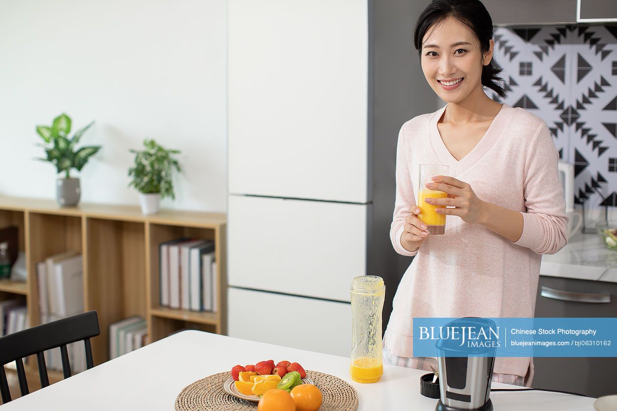 Happy young Chinese woman making juice at home