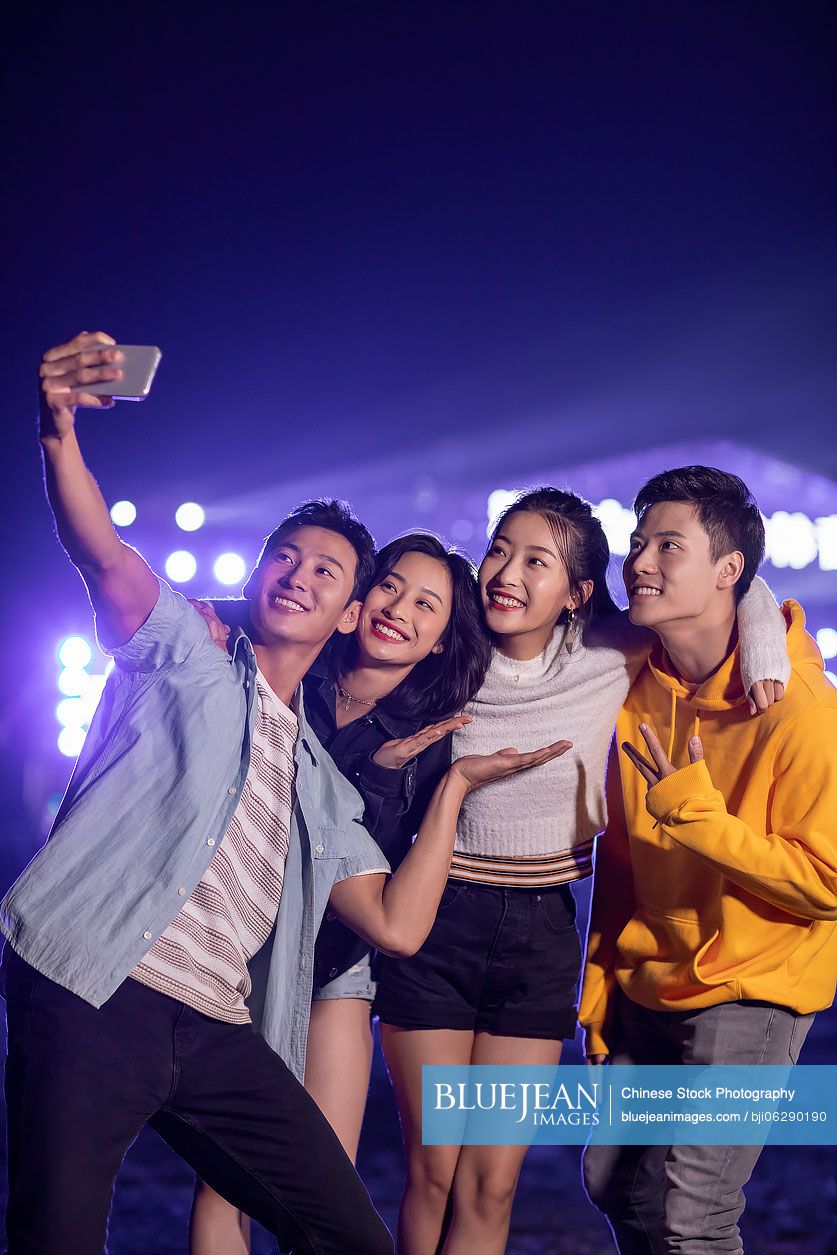 Happy young Chinese friends taking selfie at music festival