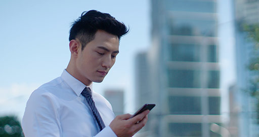 Confident young Chinese businessman using smartphone on street,4K