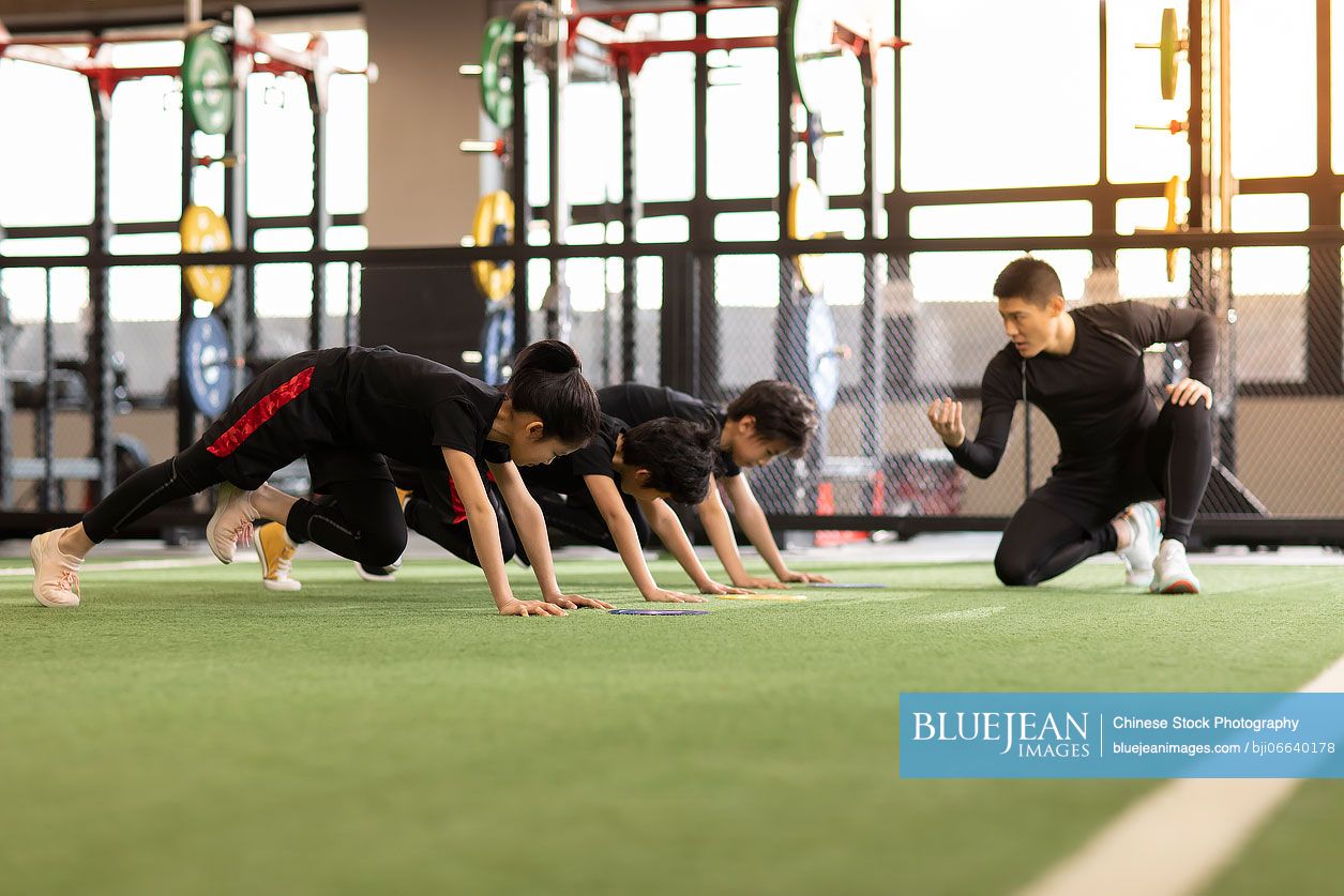 Active Chinese children having exercise class with their coach in gym