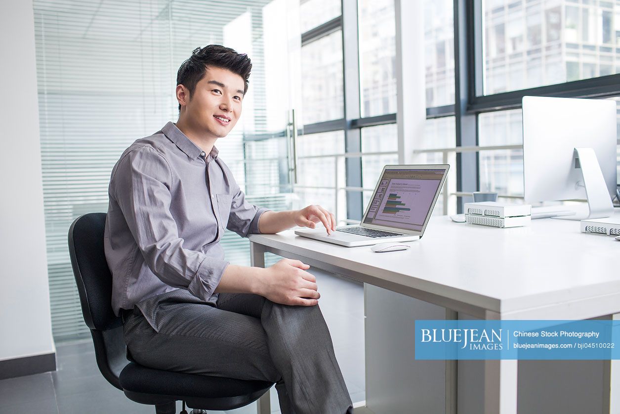 Young Chinese businessman using laptop in office