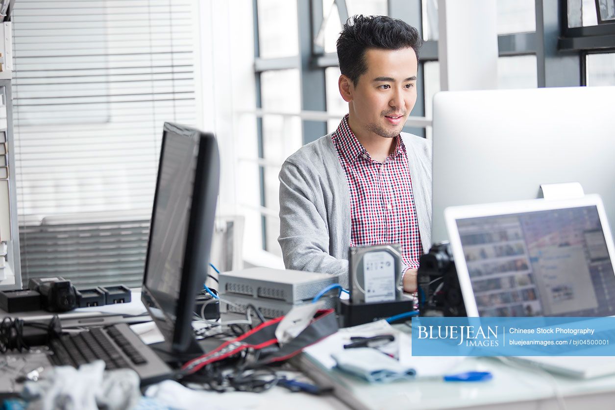 Male Chinese photographer working in office with computer