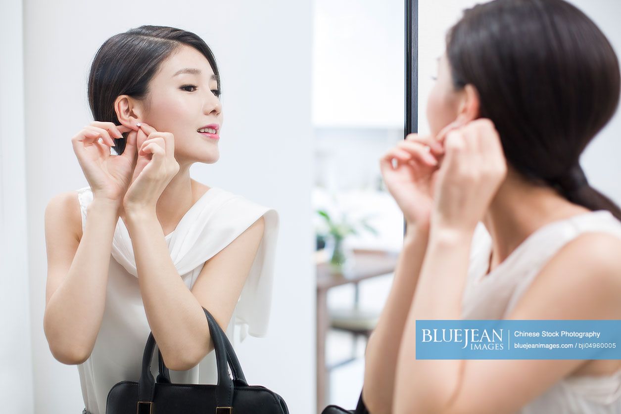 Young Chinese woman wearing earrings in front of mirror