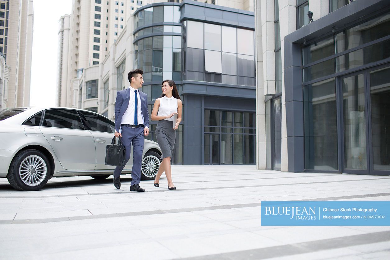 Confident Chinese business people talking and walking outdoors