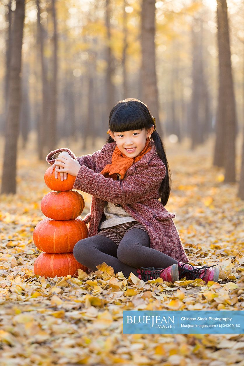 Little Chinese girl playing with pumpkins in autumn woods
