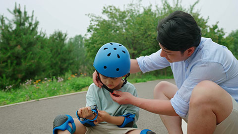 Dad assists his son with safety equipment before skateboarding