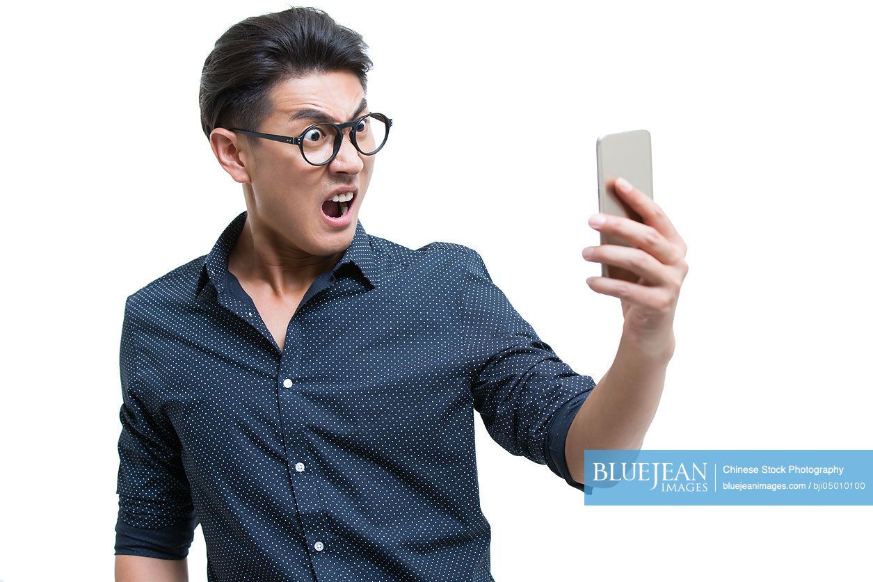 Angry young Chinese man looking at smart phone