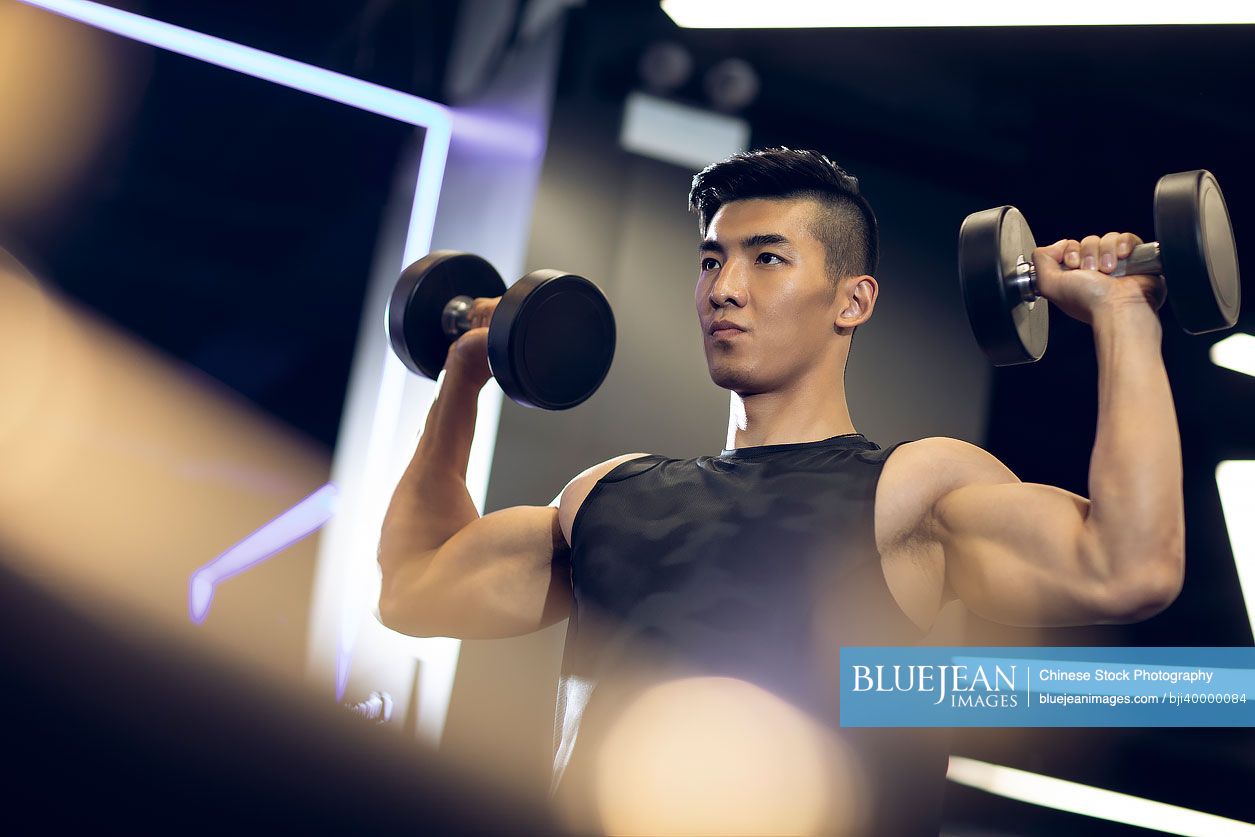 Young Chinese man working out with dumbbell at gym