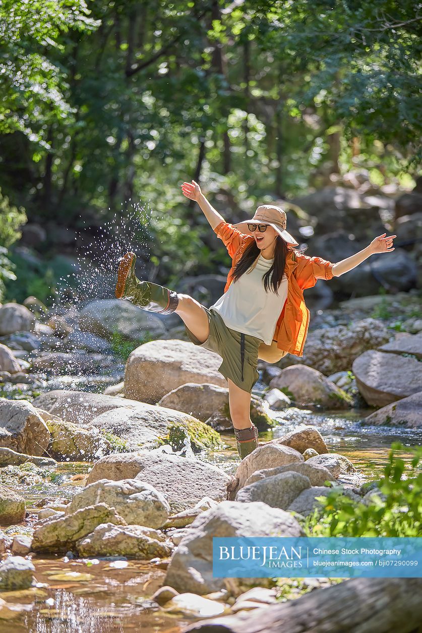 Young woman enjoying herself by the stream, wearing rain boots
