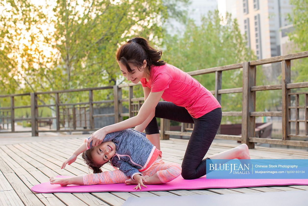 Happy Chinese mother and daughter doing yoga outdoors