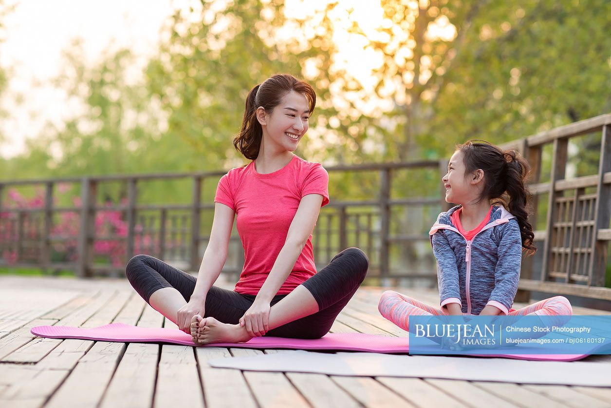 Happy Chinese mother and daughter doing yoga outdoors