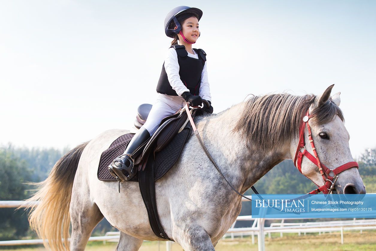 Cheerful little Chinese girl riding horse