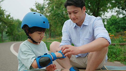 Dad assists his son with safety equipment before skateboarding