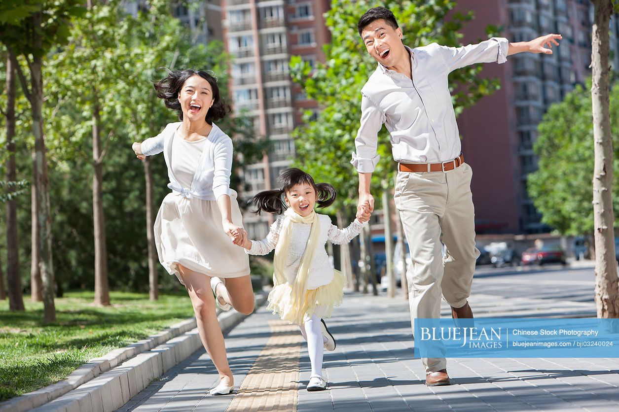 Chinese parents with daughter running on sidewalk hand in hand