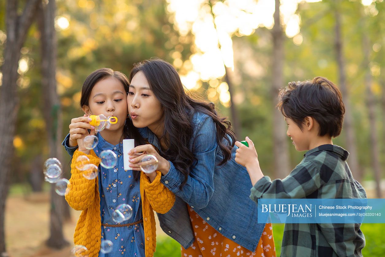 Happy young Chinese family blowing bubbles in park