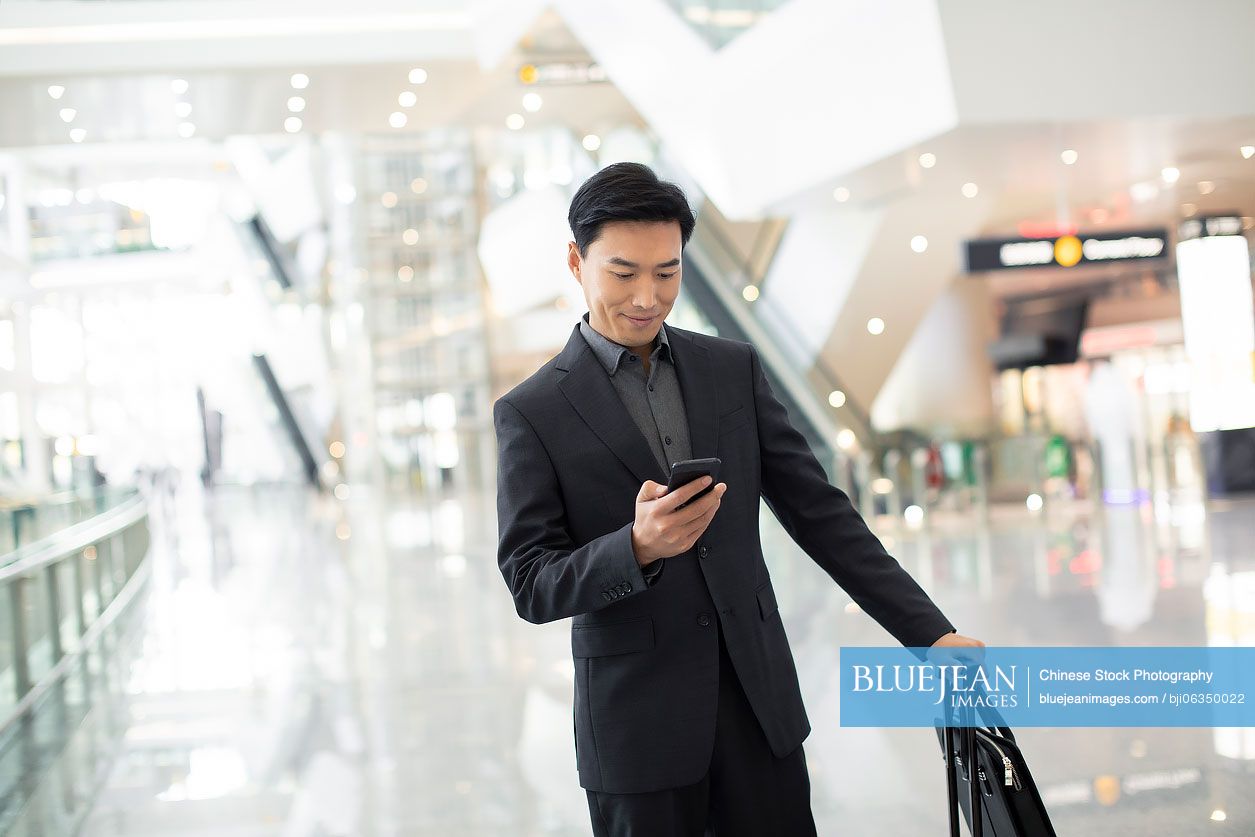 Successful Chinese businessman using smartphone at airport