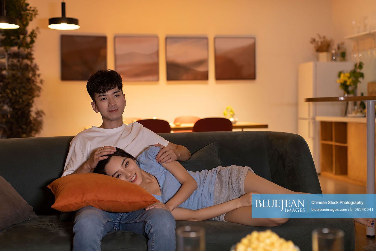 Happy young Chinese couple watching TV at home