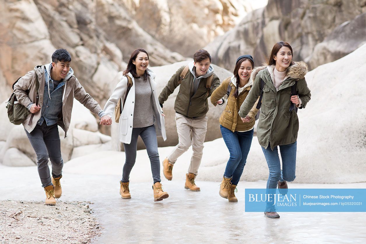 Happy young Chinese friends holding hands running outdoors in winter