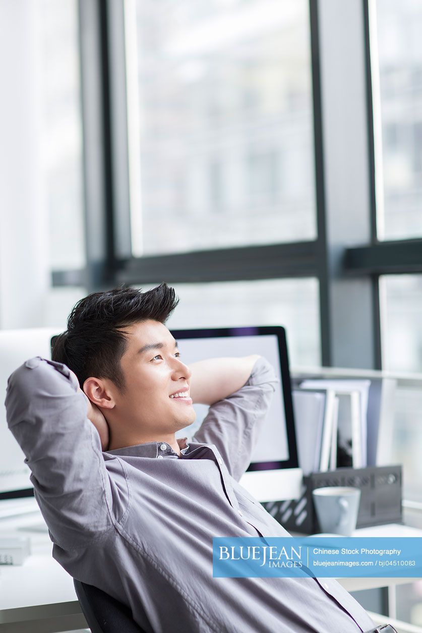 Young Chinese businessman looking through window in office