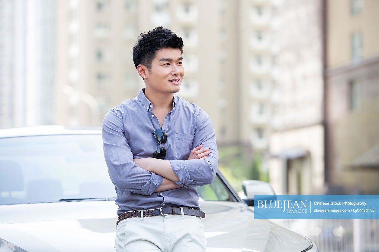 Young Chinese man leaning against his car