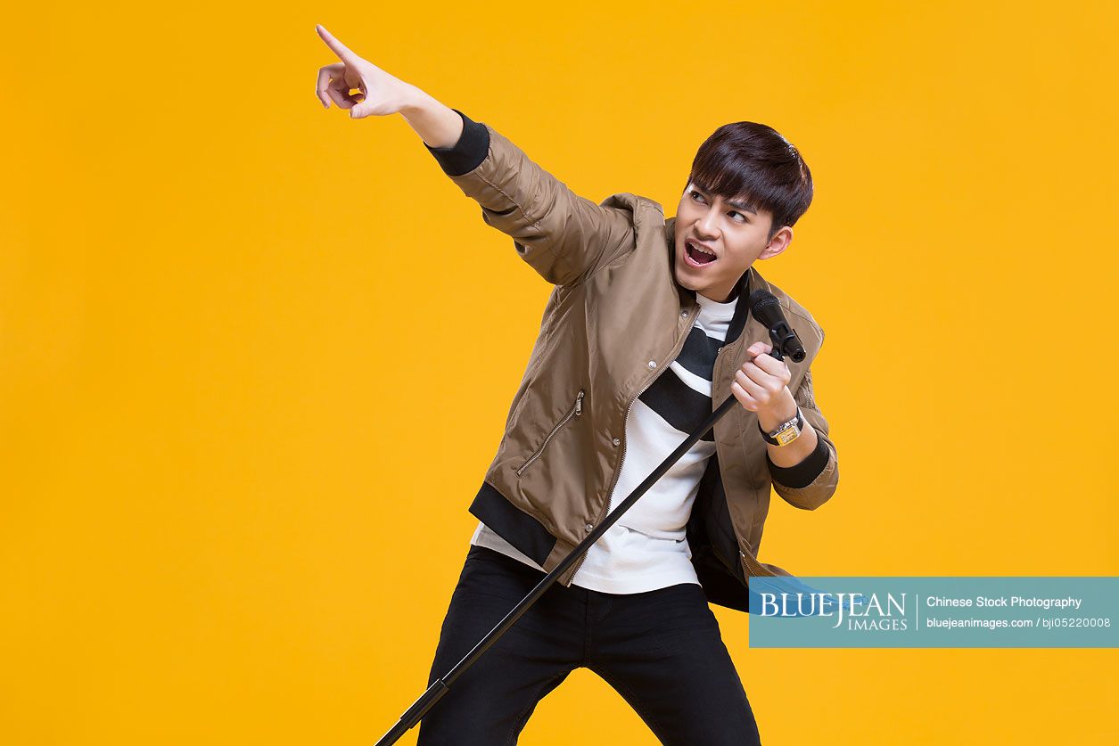 Cheerful young Chinese man singing with microphone