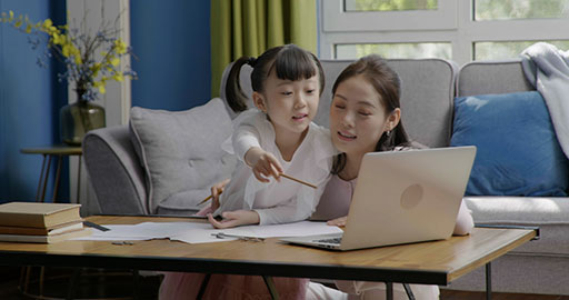 Little girl taking an online class with her mom keeping her company