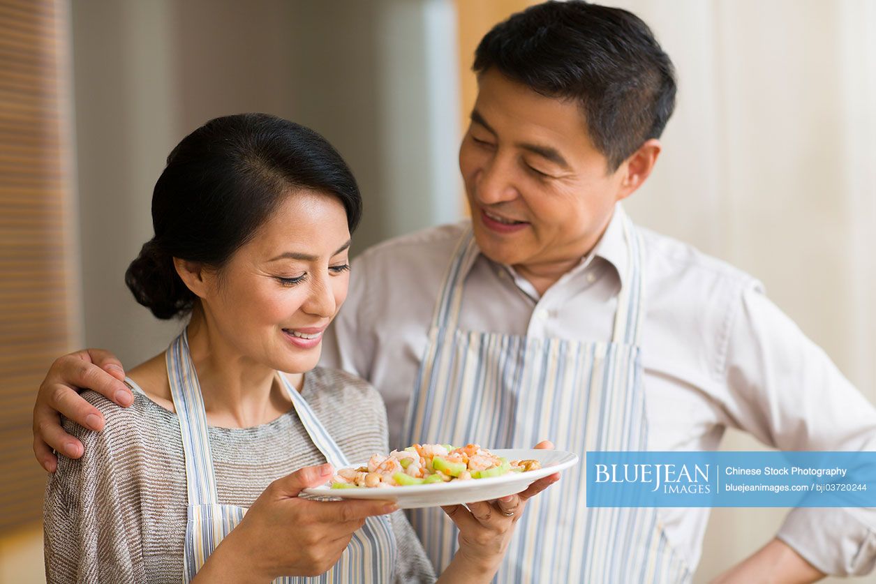 Mature Chinese couple enjoying food in kitchen