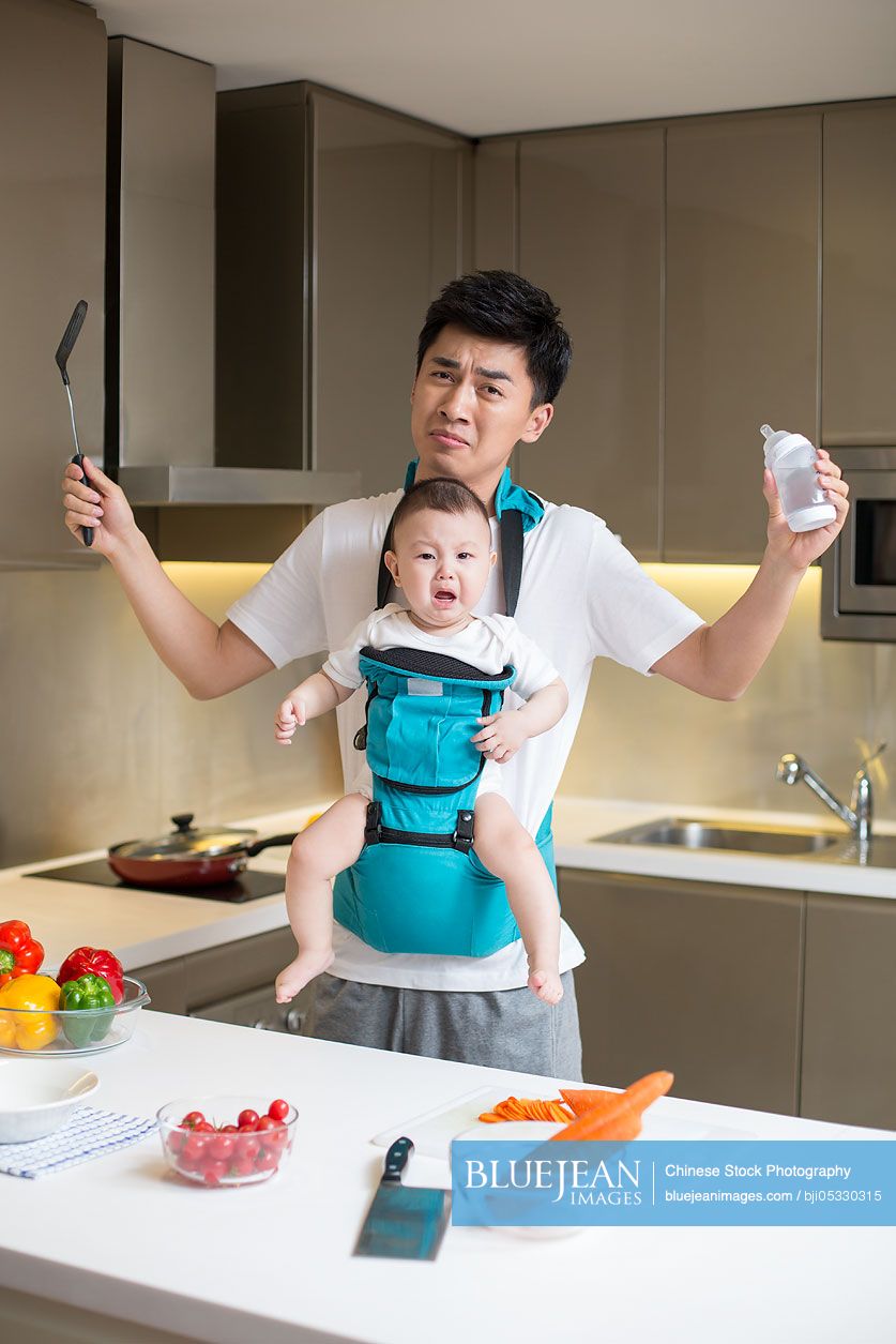 Chinese father holding baby and cooking in the kitchen