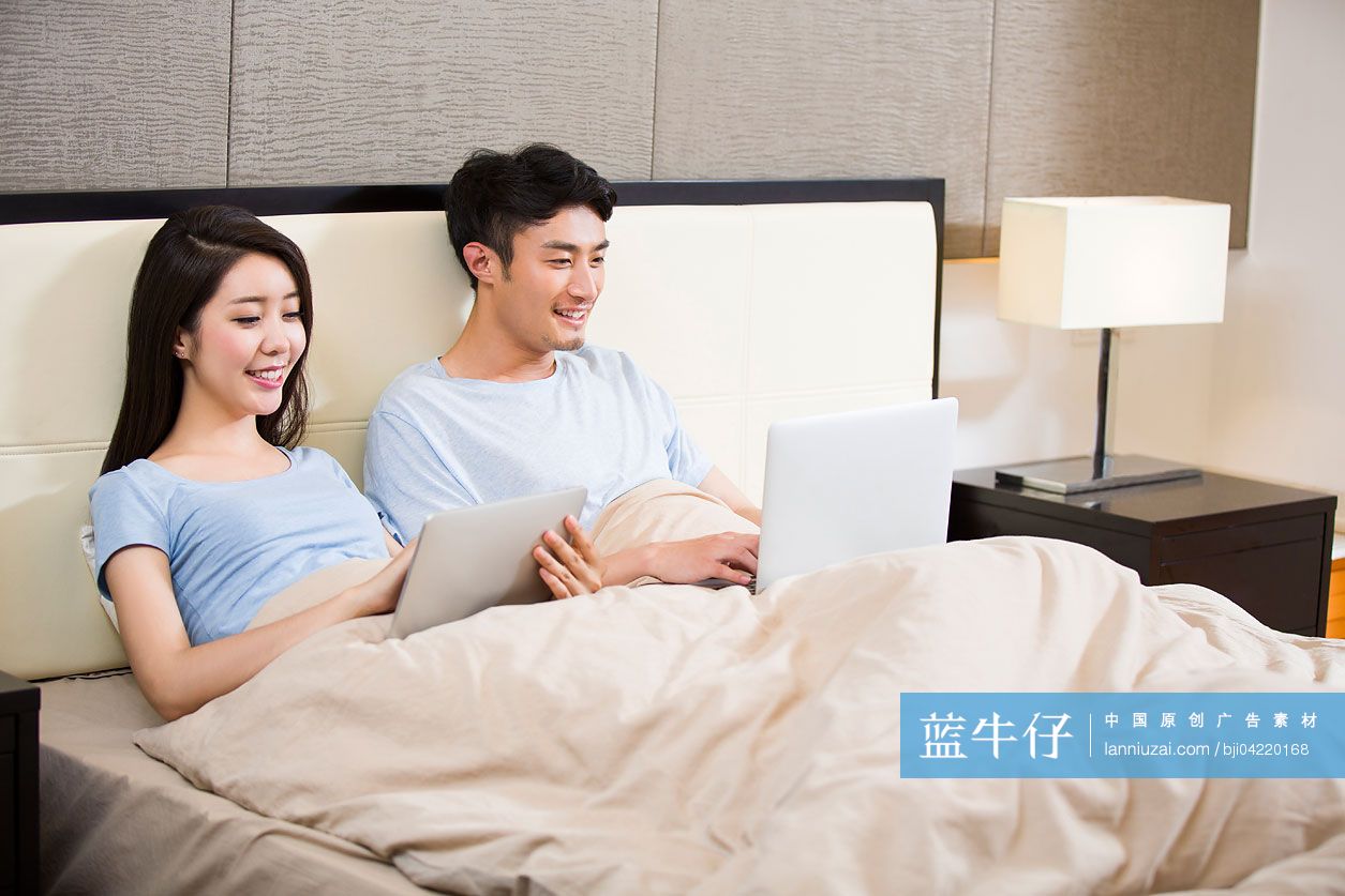 年轻夫妇在床上使用无线设备