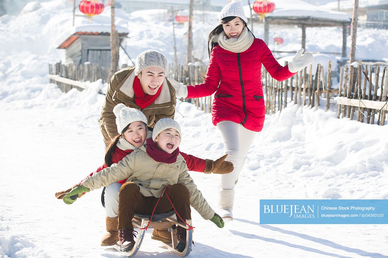 Happy Chinese family playing with sled in the snow