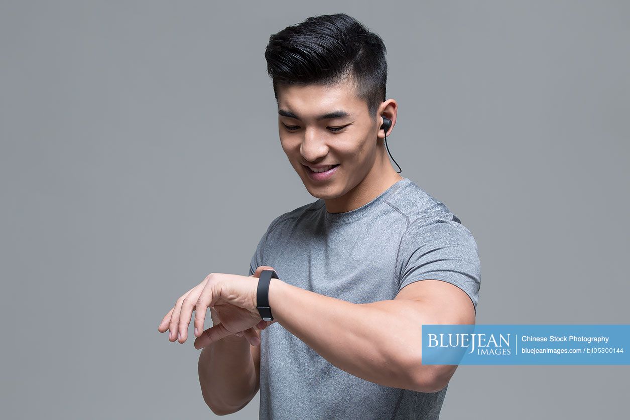 Young Chinese male athlete with headphones checking smart watch after exercising