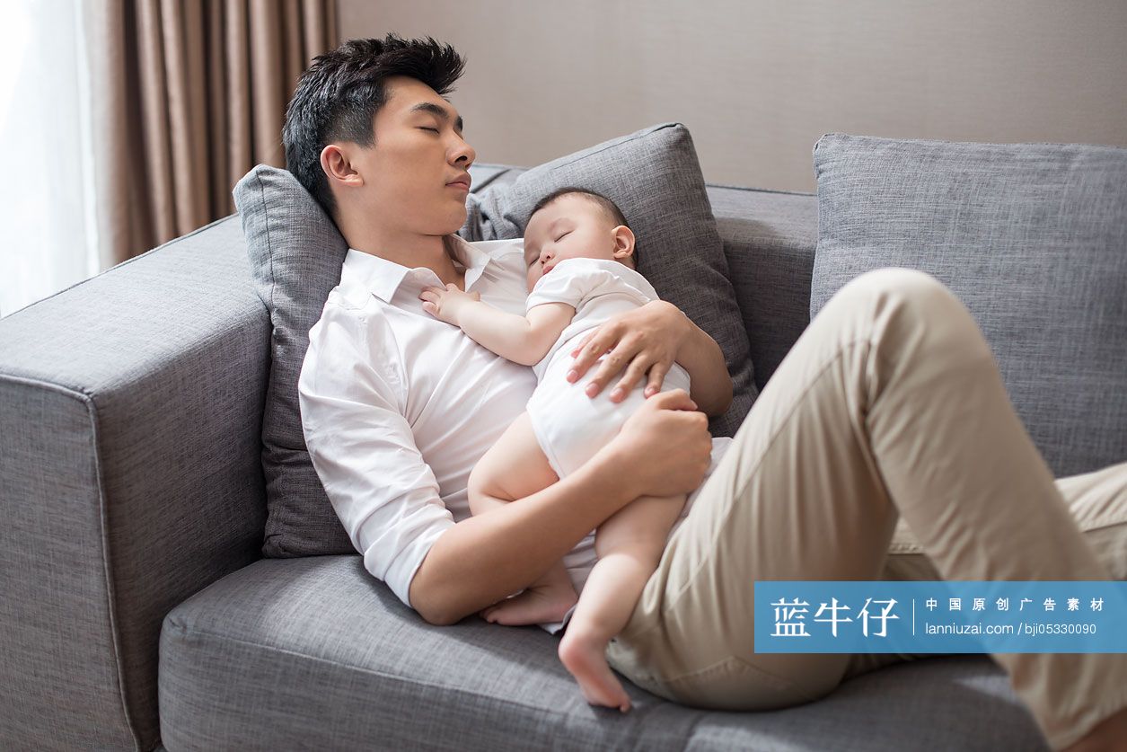 年轻爸爸抱着宝宝在沙发上睡觉