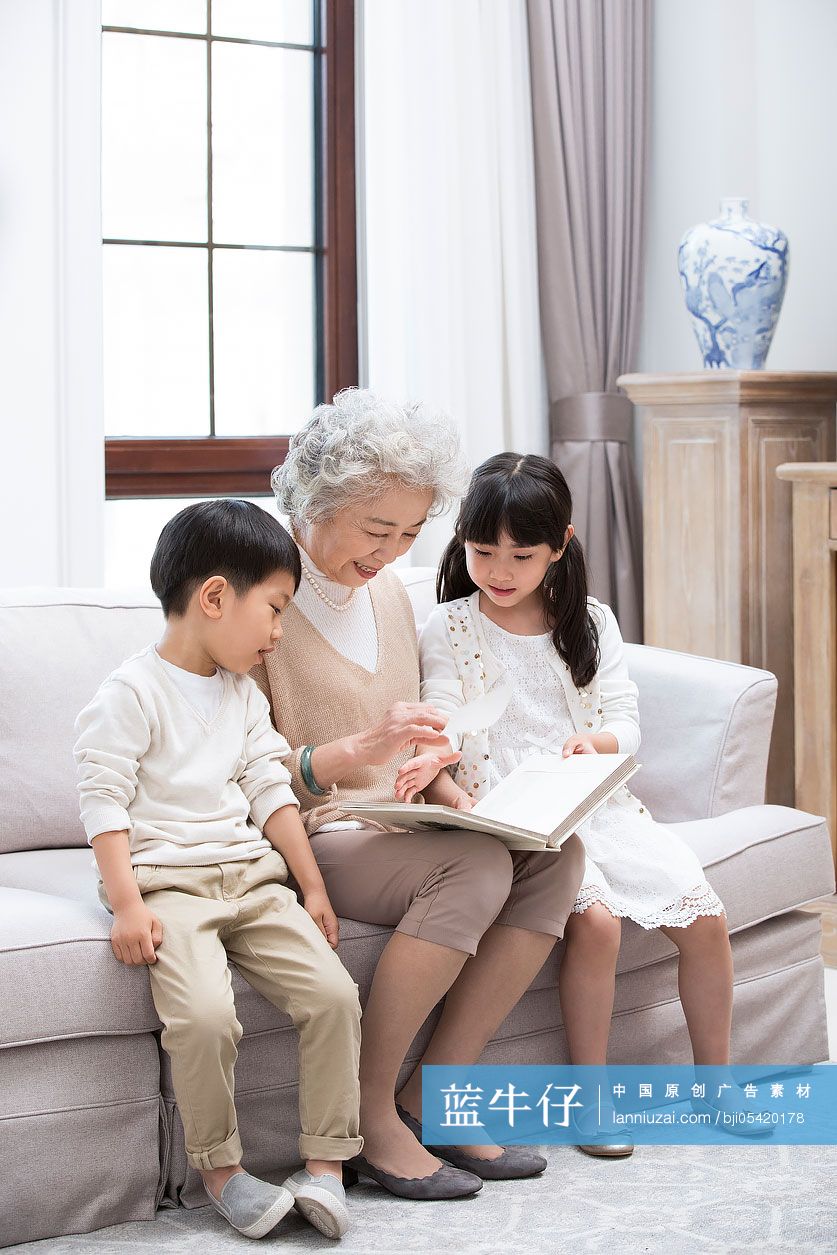 开心的奶奶和孙子孙女在沙发上看相册