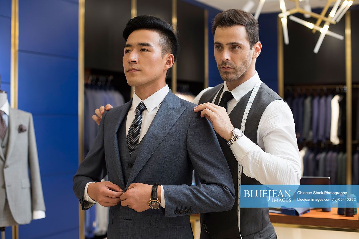 Chinese fashion designer examining suit on customer