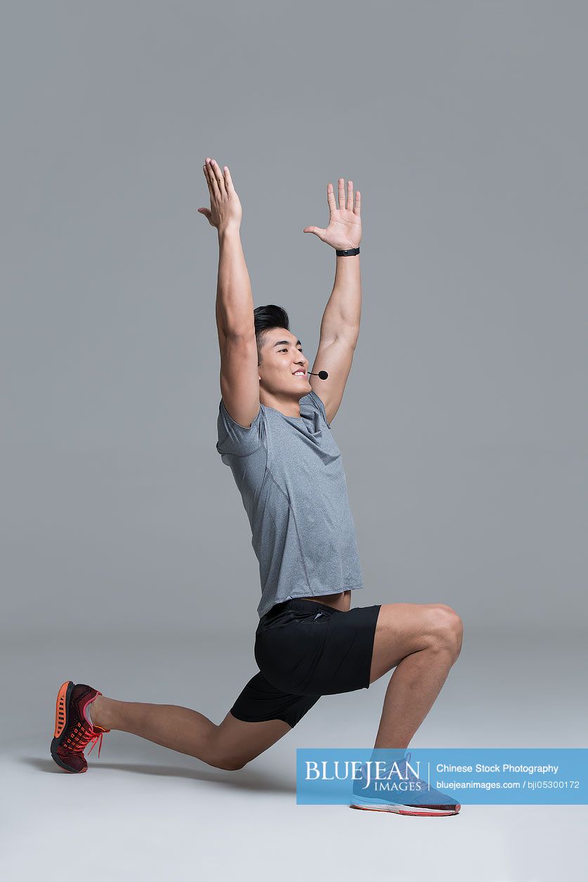 Cheerful young Chinese male trainer with headset teaching at gym