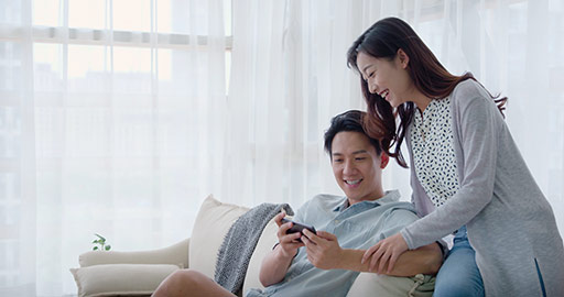 Happy young Chinese couple using smartphone in living room,4K