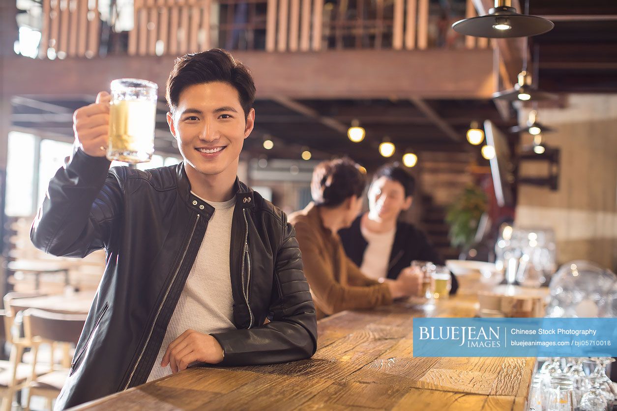 Happy young Chinese man drinking beer in bar