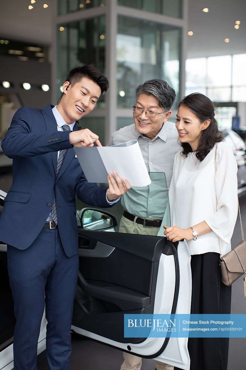 Happy mature Chinese couple choosing car in showroom
